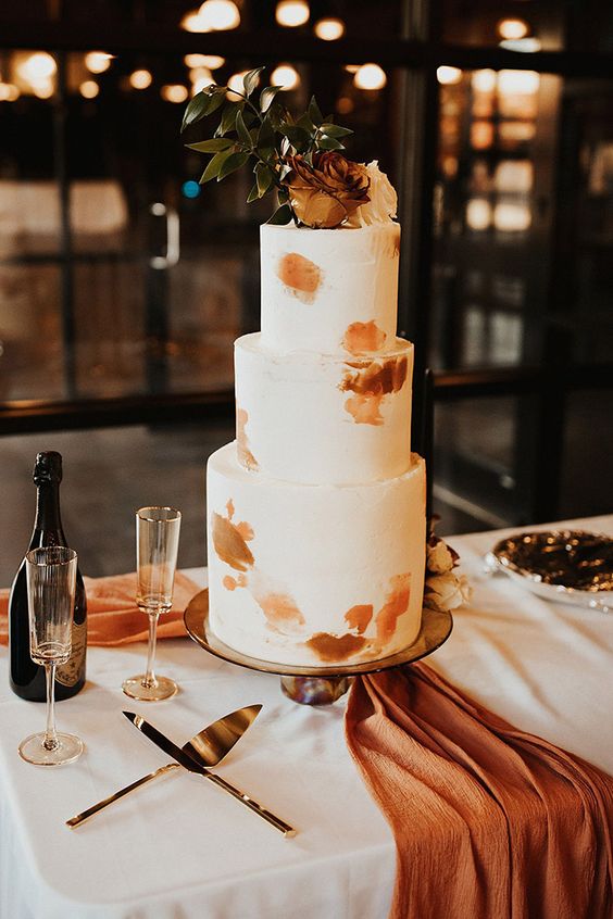 a modern to minimalist fall wedding cake with rust and orange brushstrokes and some matching blooms on top