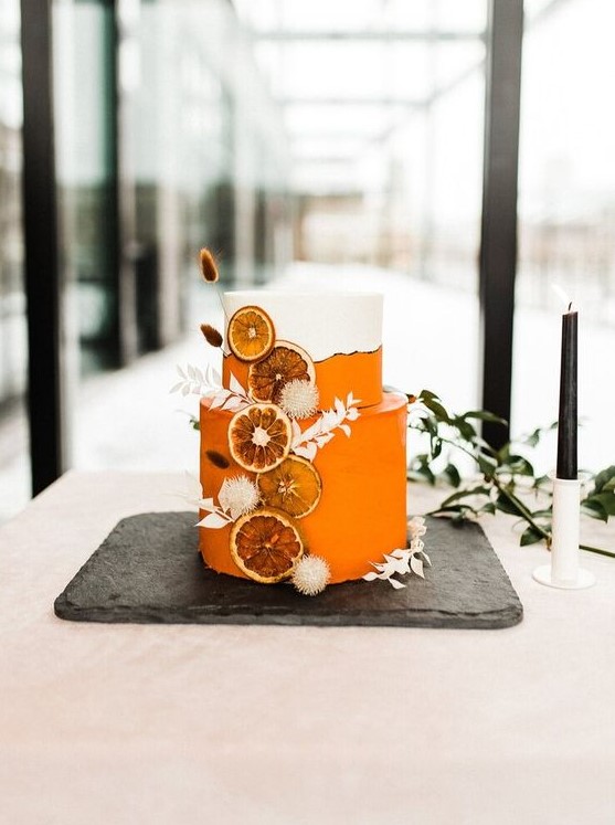 a stunning white and orange wedding cake with white dried grasses and dried citrus slices is a lovely idea for a tropical boho wedding