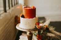 52 a two tone wedding cake with a rough edge, with a white and rust tier, gold leaf and fresh bright blooms and greenery