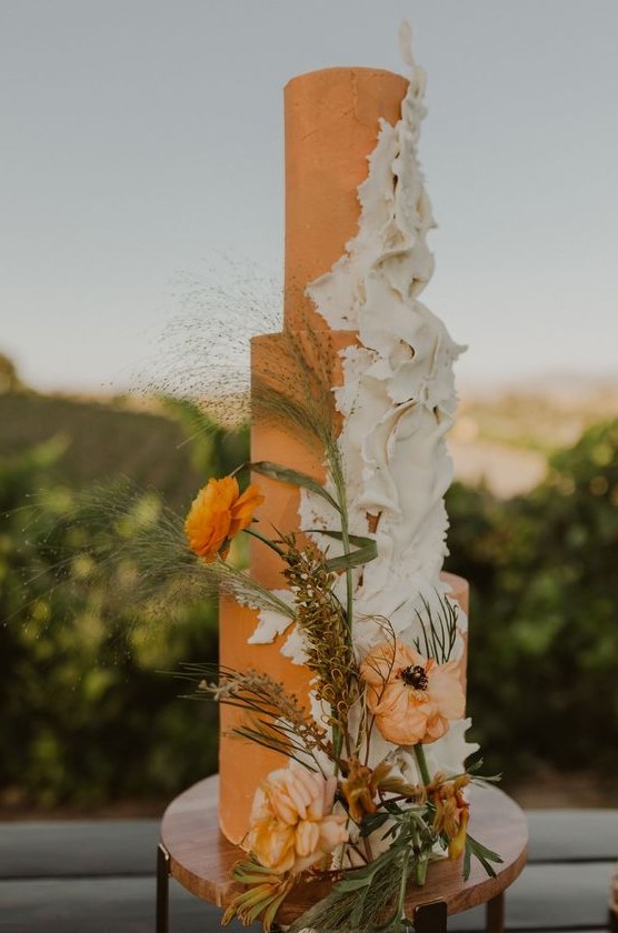 an orange wedding cake with white sugar ruffles, orange blooms and dried herbs plus greenery is chic