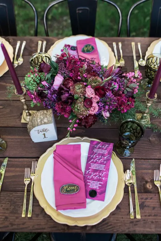 a beautiful berry-tone wedding centerpiece with deep purple, pink, purple blooms, greenery and matching purple candles