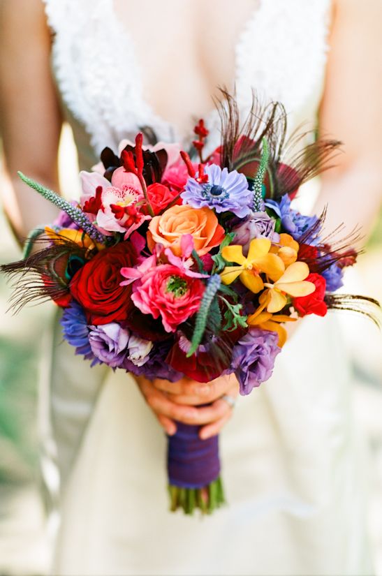 a bold jewel tone wedding bouquet with deep red, pink, purple, blue and burgundy blooms, greenery and peacock feathers