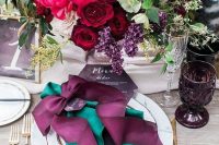 a bold jewel tone wedding centerpiece of burgundy, hot pink, purple, neutral blooms, greenery and grasses and matching place setting styling