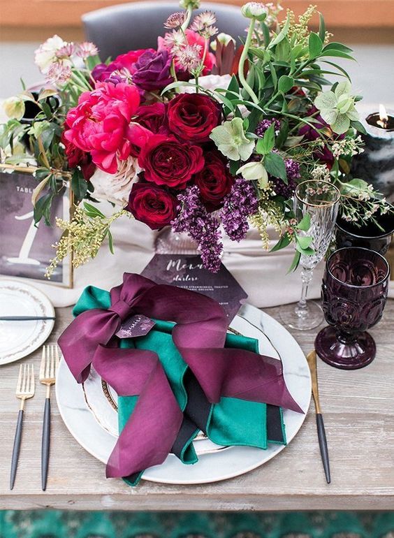 a bold jewel tone wedding centerpiece of burgundy, hot pink, purple, neutral blooms, greenery and grasses and matching place setting styling