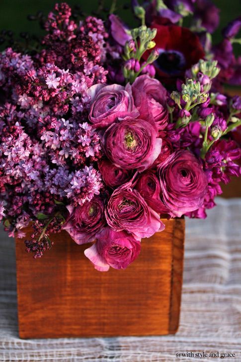 a bold jewel tone wedding centerpiece of purple ranunculus, lilac and some other blooms in a wooden box is wow