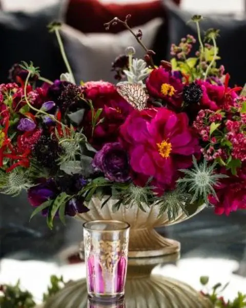 a bold jewel tone wedding centerpiece of violet, fuchsia, purple and deep red blooms, thistles, greenery and plenty of texture