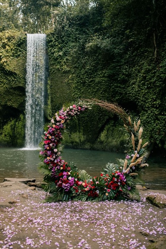 a bold tropical wedding arch with fronds, pampas grass, hot pink, red and blush blooms is a pretty idea for a boho wedding