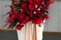 a breathtaking jewel tone wedding bouquet with deep red, burgundy and purple blooms, foliage and greenery and long ribbon