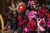 a breathtaking jewel tone wedding centerpiece of depe red, pink and lamost black blooms, a bit of greenery and berries for the fall