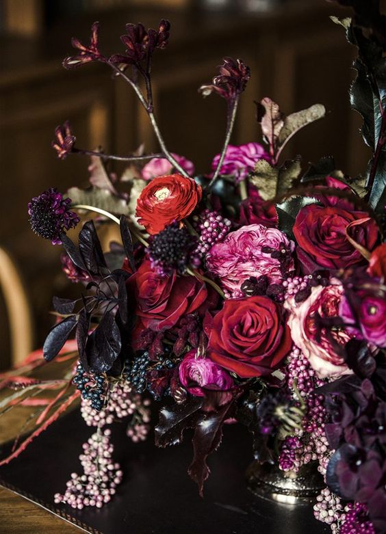 a breathtaking jewel tone wedding centerpiece of depe red, pink and lamost black blooms, a bit of greenery and berries for the fall