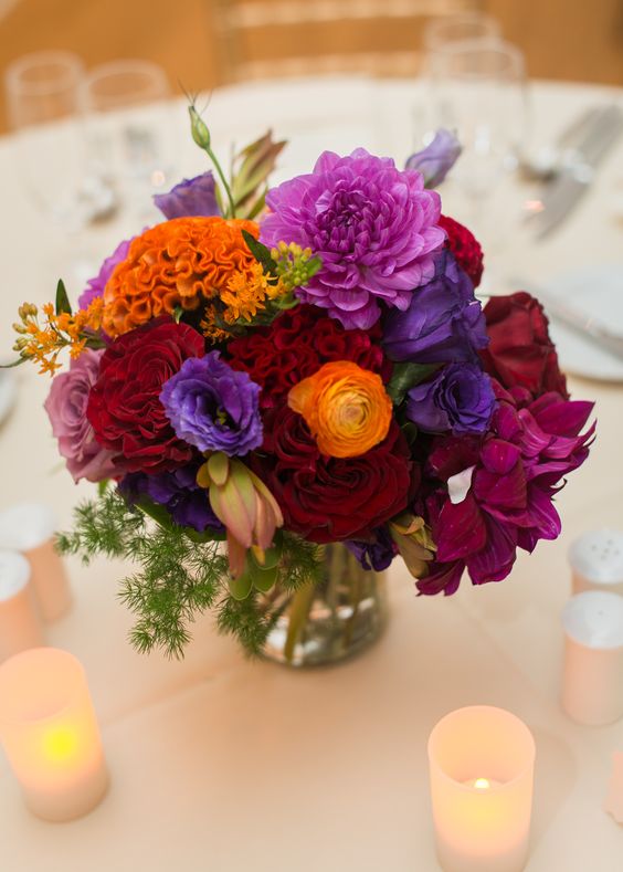 a bright jewel tone wedding centerpiece of orange, purple, violet, burgundy and fuchsia blooms and some greenery
