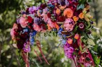 a colorful wedding arch in jewel tones – burgundy, deep red, orange, yellow and pink blooms and greenery is a chic idea for a fall wedding