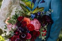 a deep tone bridal bouquet with burgundy anemones, burgundy roses, pink peonies, blue and deep purple blooms and greenery