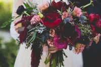 a deep tone wedding bouquet with burgundy peonies, pink and hot pink blooms, blue thistles, lisianthus and some foliage