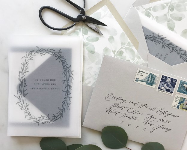 a delicate neutral wedding invitation suite with a grey envelope with botanical lining, a vellum jacket with a print