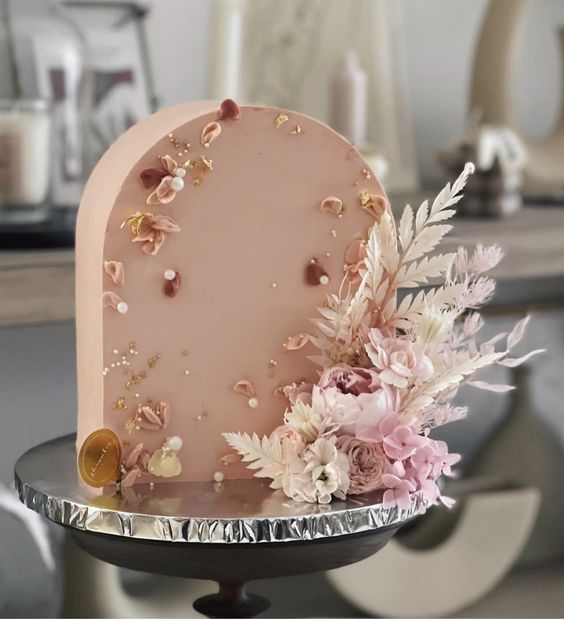 a dusty pink arch wedding cake decorated with sugar and real petals, pearls, dried and fresh blooms in pink and white looks very sophisticated