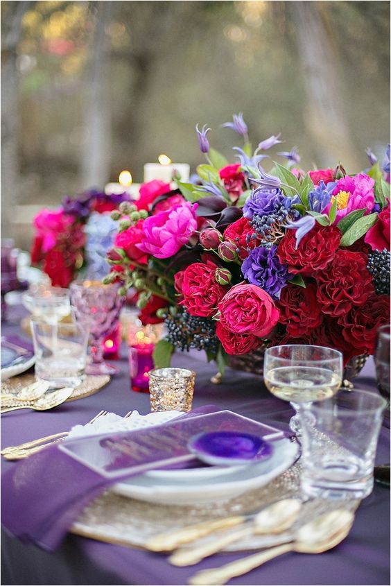a fab jewel tone wedding centerpiece of red, deep red, hot pink, violet blooms, privet berries and greenery is a chic idea