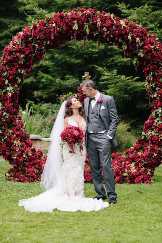 a fantastic round wedding arch covered with deep red and burgindu blooms and greenery for a bright fall wedding