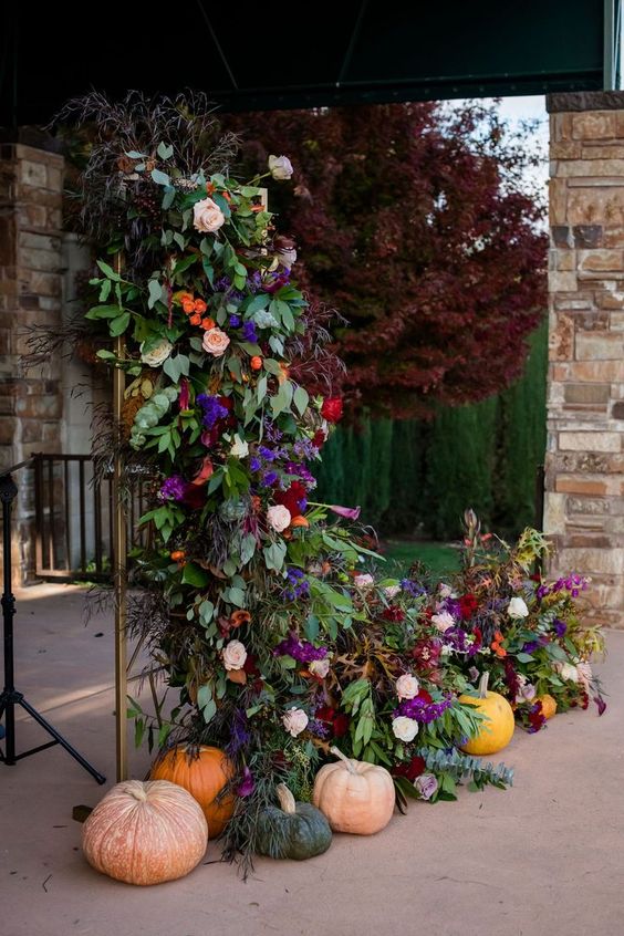 a fantastic wedding backdrop of a floral arrangement with violet, blush, burgundy and orange blooms, lush foliage and greenery and pumpkins