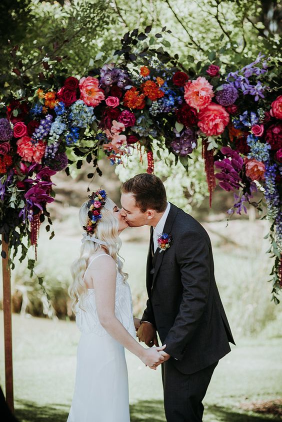 a gorgeous bold wedding arch with blue, purple, burgundy, hot red and lilac blooms and greenery for the fall