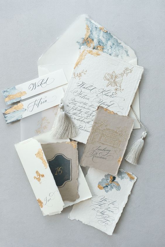 a gorgeous handmade paper wedding invitation suite with blue watercolors, gold foil and a torn edge plus tassels