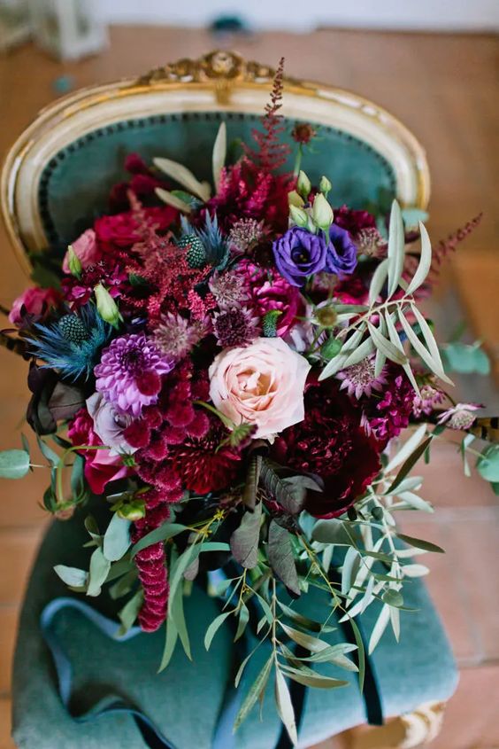 a gorgeous wedding bouquet of burgundy, violet, deep purple and pink blooms, blue thistles and greenery for the fall