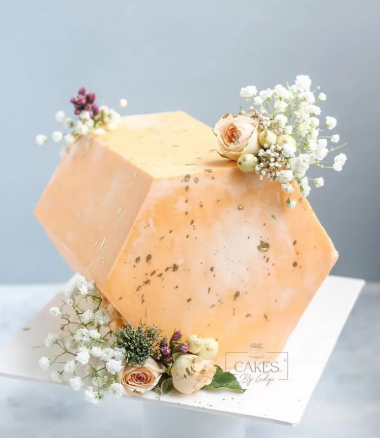 a hexagonal orange cake top forward wedding cake decorated with baby's breath and some roses plus gold foil is amazing for an elegant art deco wedding