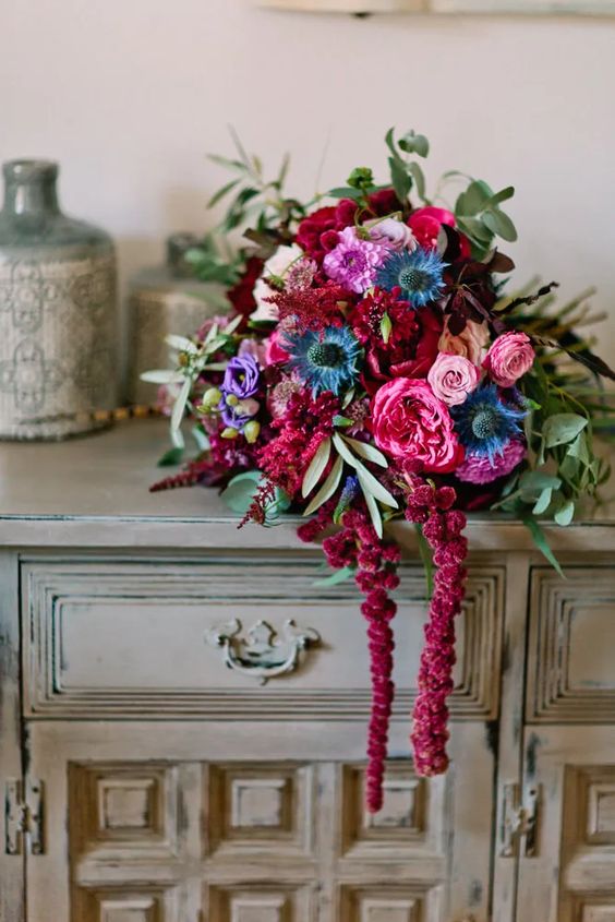 a jewel tone wedding bouquet of burgundy, pink and blue and purple blooms, greenery, amaranthus and thistles
