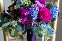 a jewel-tone wedding bouquet with hot pink and pink roses, purple, bold blue blooms, pale greenery and privet berries