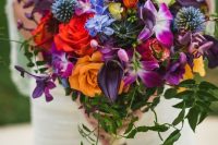 a jewel-tone wedding bouquet with red, yellow, purple and blue flowers, allium, thistles and greenery for a fall wedding