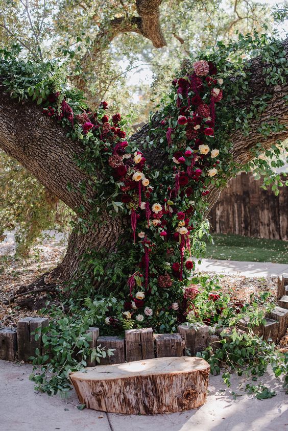 a living tree wedding altar with greenery, peachy and burgundy blooms, lisianthus and amaranthus is a gorgeous idea for a jewel tone wedding