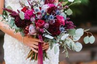 a lovely jewel tone wedding bouquet with hot pink, purple, burgundy blooms, blue thistles and greenery for a fall wedding