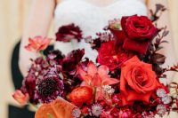 a lovely modern wedding bouquet with deep red, burgundy and purple blooms, an orange piece is wow