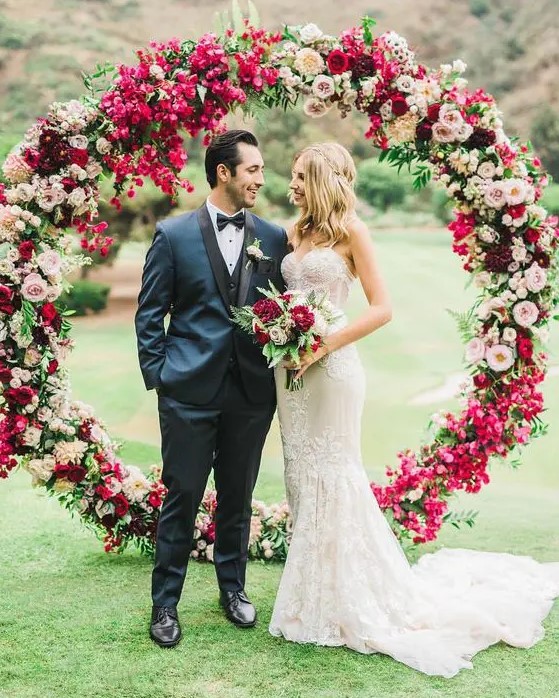 a lush circle wedding arch with fuchsia, red, pink and burgundy blooms for a colorful wedding