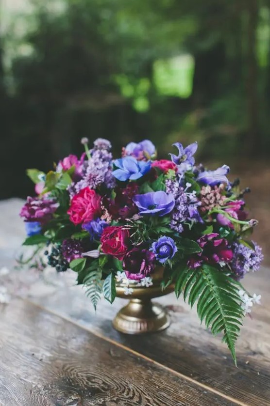 a lush floral wedding centerpiece with violet, fuchsia and burgundy flowers in a gold vase is a wow idea