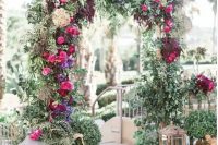 a lush greenery wedidng arch with fuchsia, violet and burgundy blooms and super lush greenery surrounded with candle lanterns and potted plants