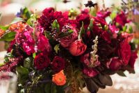 a lush jewel tone wedding centerpiece of fuchsia, deep red, burgundy and orange blooms and greenery for the fall