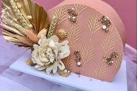 a mauve wedding cake with sugar patterns, gold and white pearls and some blooms, dried and fresh ones, with a gold frond