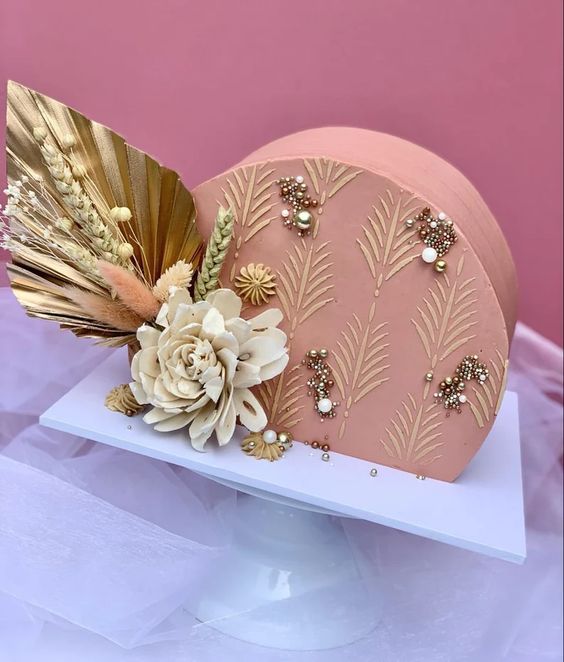 a mauve wedding cake with sugar patterns, gold and white pearls and some blooms, dried and fresh ones, with a gold frond