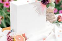 a minimalist rectangular wedding cake with grey and pink sunburst in the top right corner looks beautiful against the pure white icing and some mauve blooms