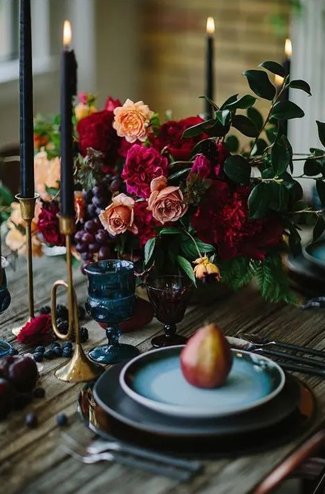 a moody wedding centerpiece with orange and burgundy blooms and grapes for a dark wedding