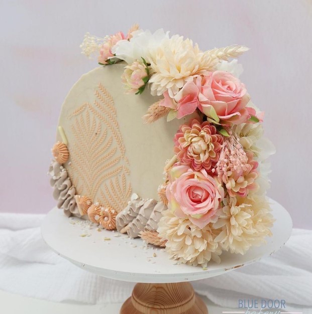 a neutral cake top forward wedding cake decorated with sugar patterns and fresh ivory and pink blooms and greenery is great for spring or summer