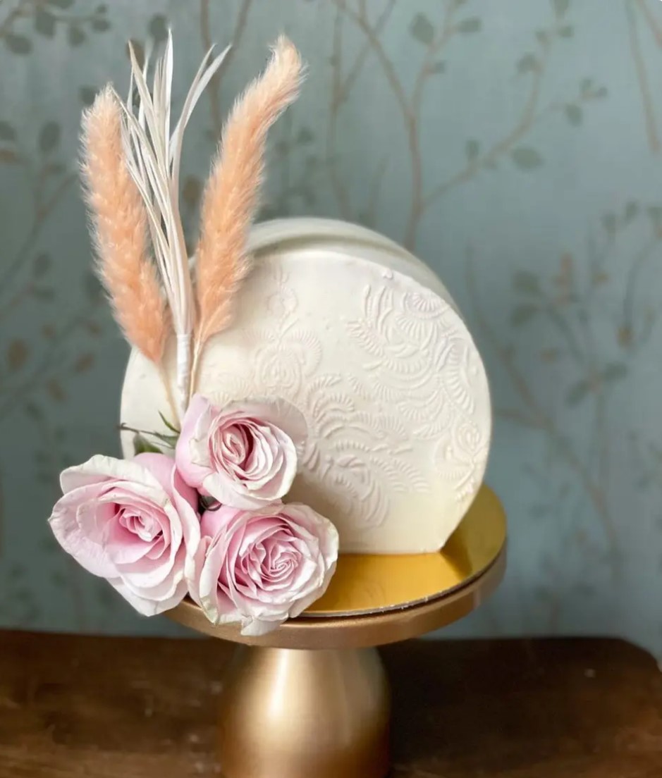 A neutral lace effect buttercream decorated with pink roses and peachy grasses is a great and chic idea for a refined vintage inspired wedding