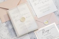 a pastel wedding invitation suite with peachy envelopes and white seals with gold, modern callgiraphy invitations and a blank vellum jacket