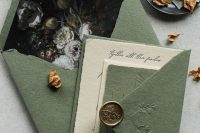 a pretty sage green wedidng invitation suite with an envelope with dark floral lining, a layered invite and a copper seal