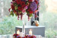 a refined jewel tone tall wedding centerpiece of violet, burgundy, pink and purple blooms, greenery and grapes