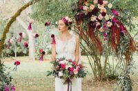 a round wedding arch decorated with moss, greenery and bold purple, burgundy, pink and deep red blooms and foliage