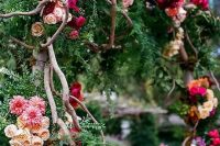 a secret garden wedding arch decorated with greenery and evergreens, bold blooms in hot pink, purple, burgundy, blush blooms and branches weaving the arch