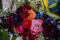 a super bold jewel tone wedding bouquet of pink, depe red, peachy, deep purple and violet blooms and greenery for the fall