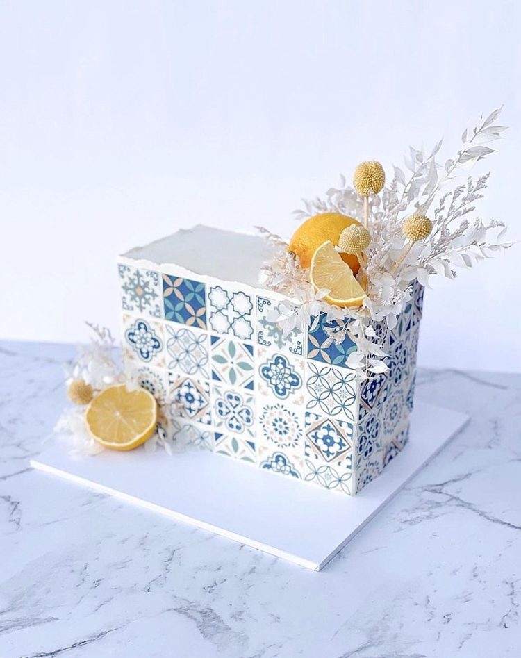 an Amalfi coat inspired rectangle wedding cake with azulejo blue tiles printed, lemons, white dried grasses and billy balls for an Italian wedding
